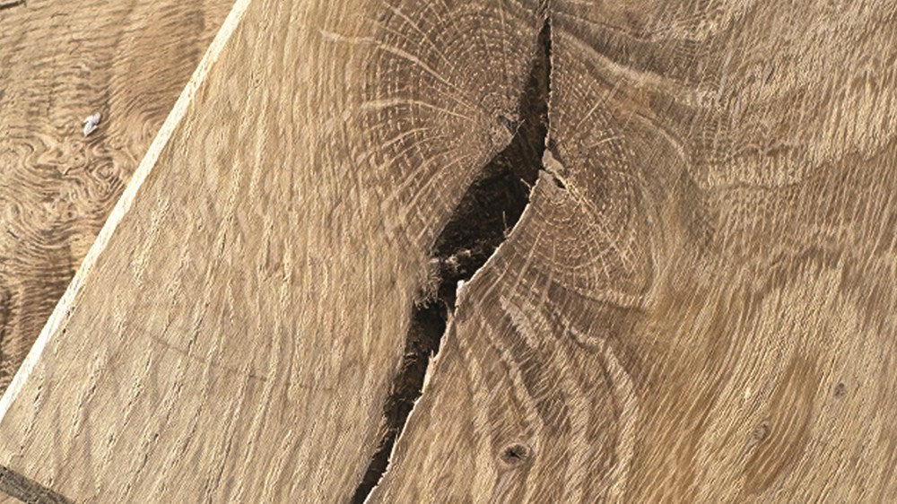 Oak board before repair, with a raw chipped-out knot and a deep open gap in the grain